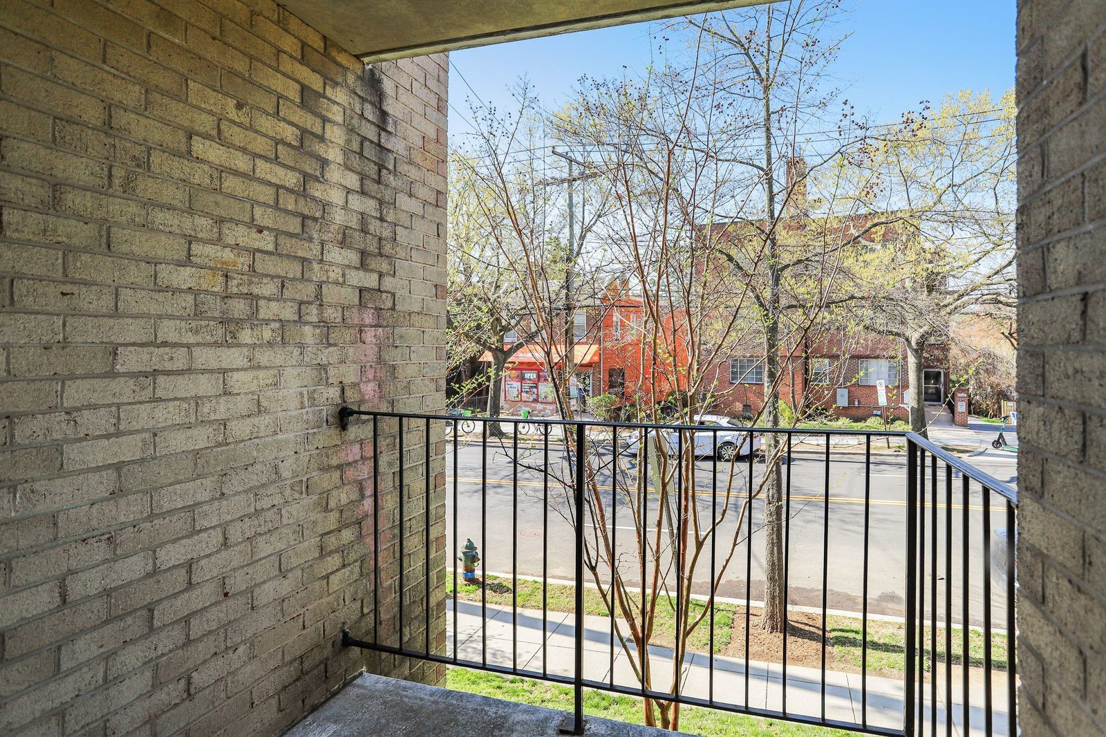 Covered brick balcony with iron railing overlooking tree-lined street