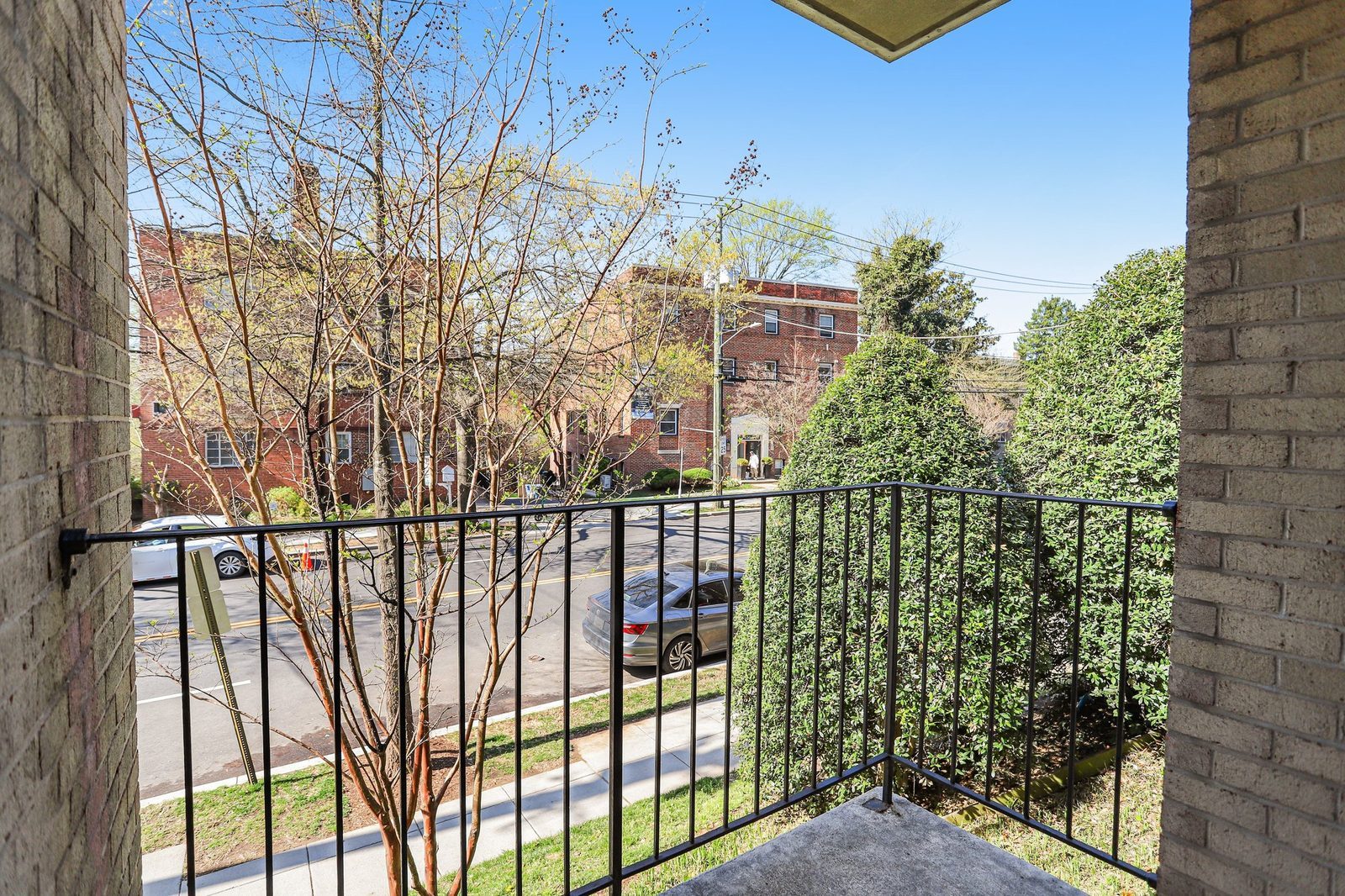 Balcony view over street toward brick buildings and hedges