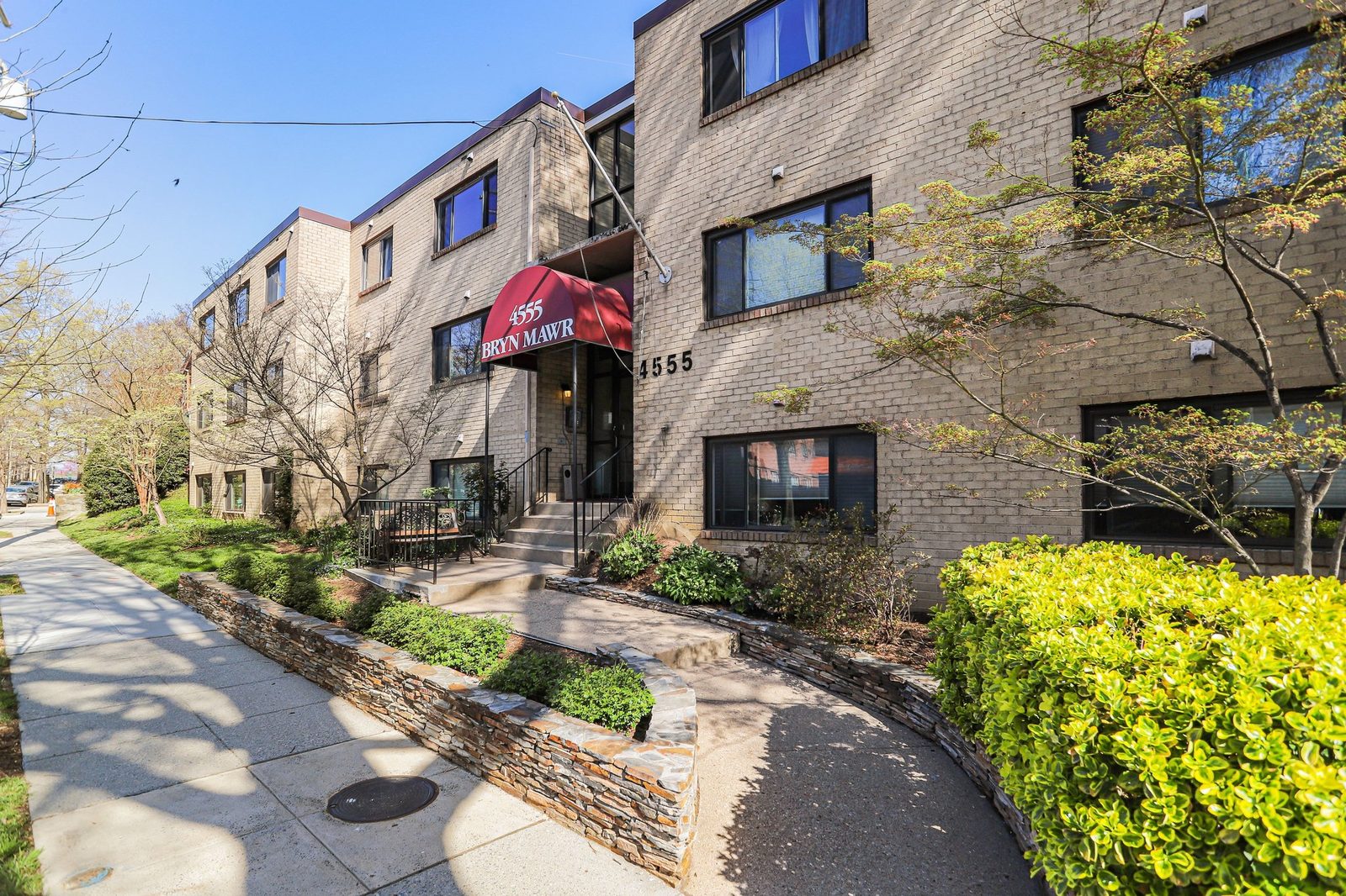 Brick condominium building entrance with red awning and stone planters