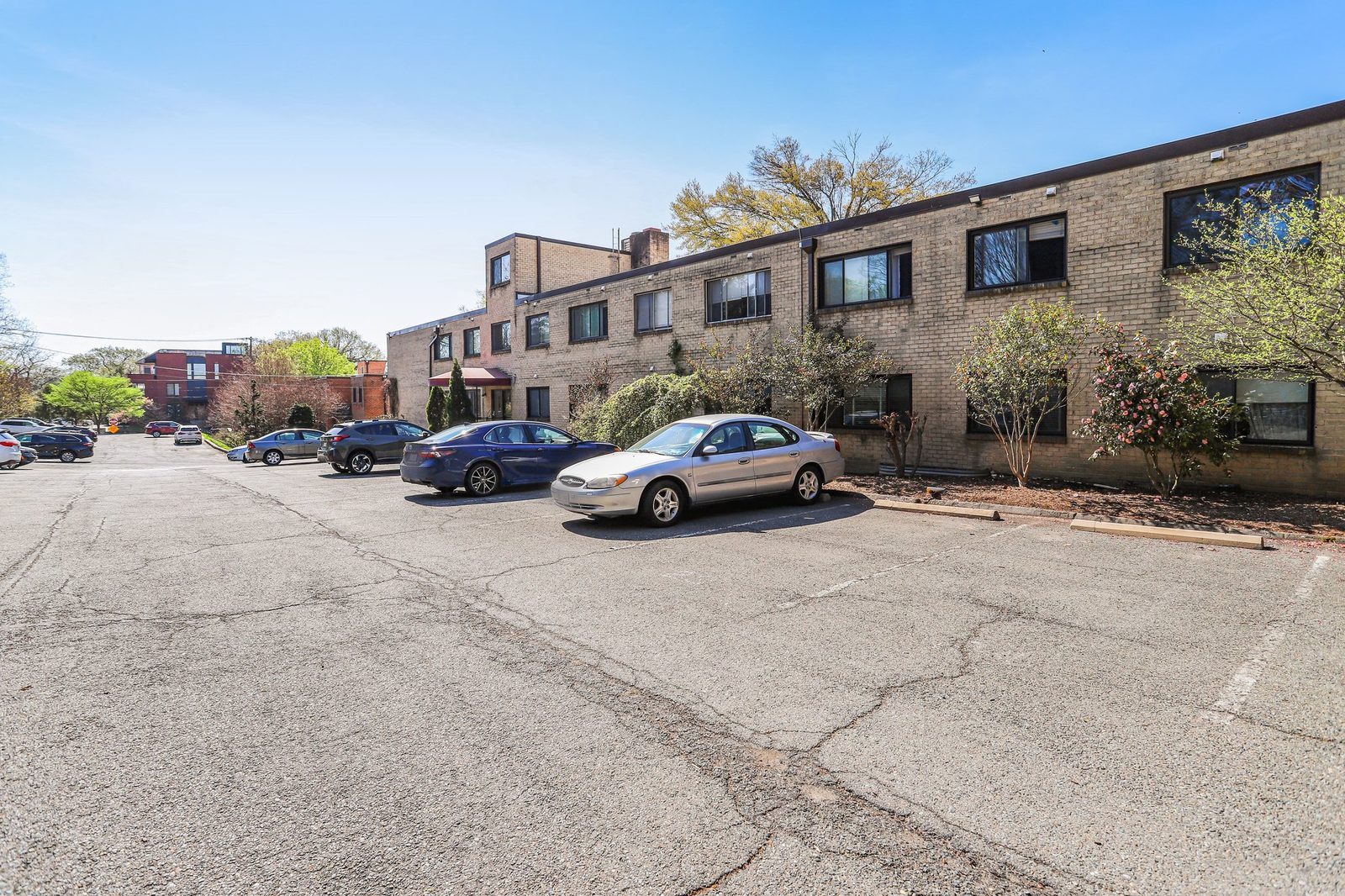 Paved parking lot along brick building with flowering shrubs