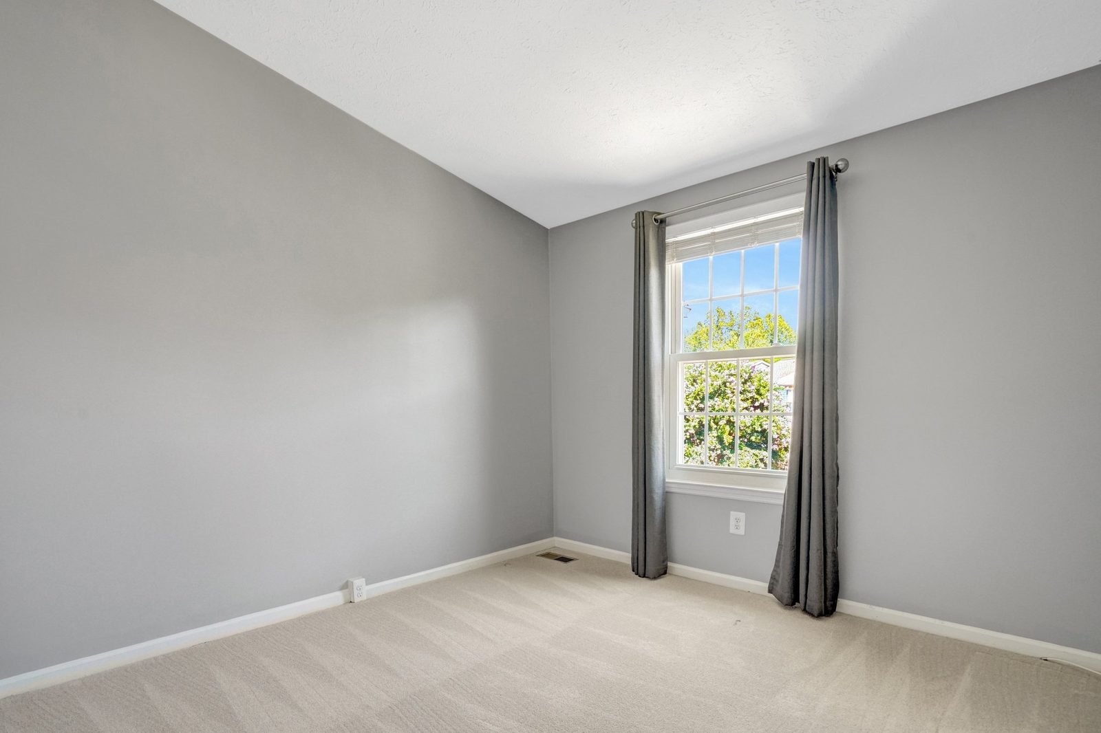 Empty carpeted room with single window and grey curtain panels