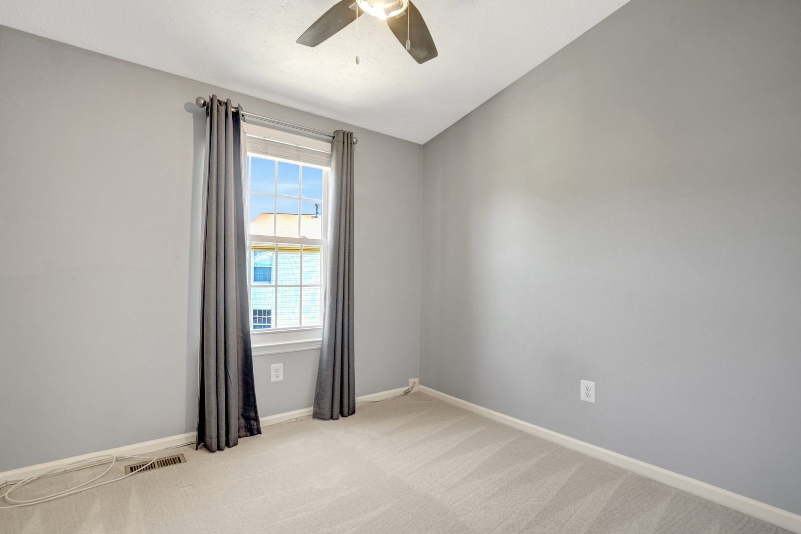 Carpeted room with ceiling fan and curtained double-hung window