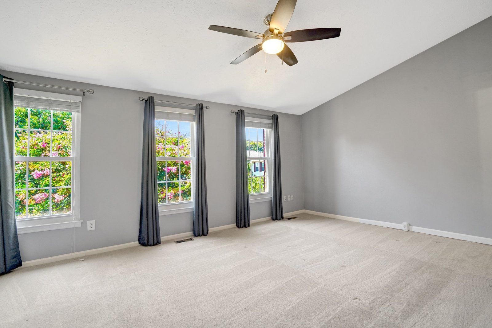Large carpeted room with three windows and ceiling fan