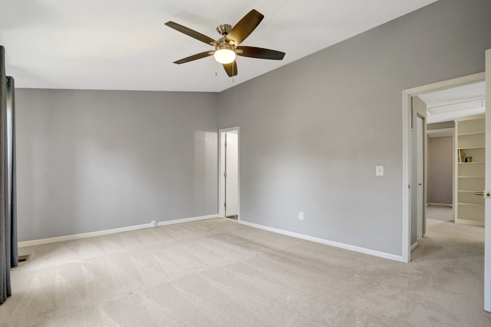 Carpeted room with ceiling fan and doorway to hall