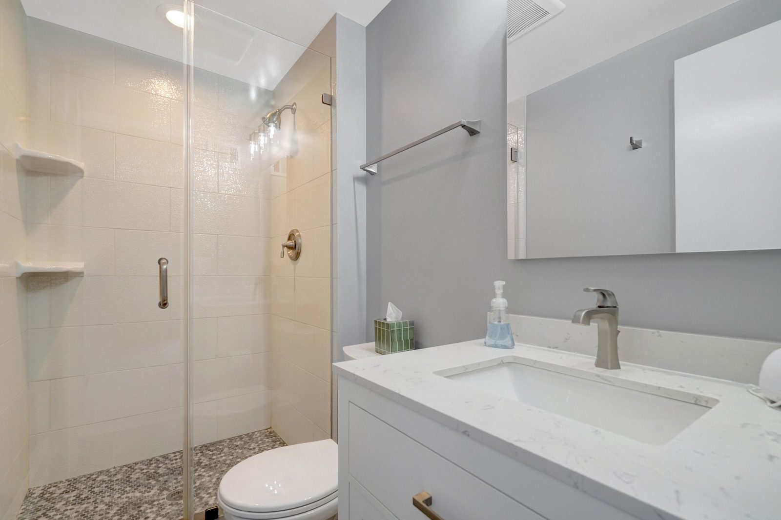 Bathroom with glass shower door, mosaic floor tile and white vanity