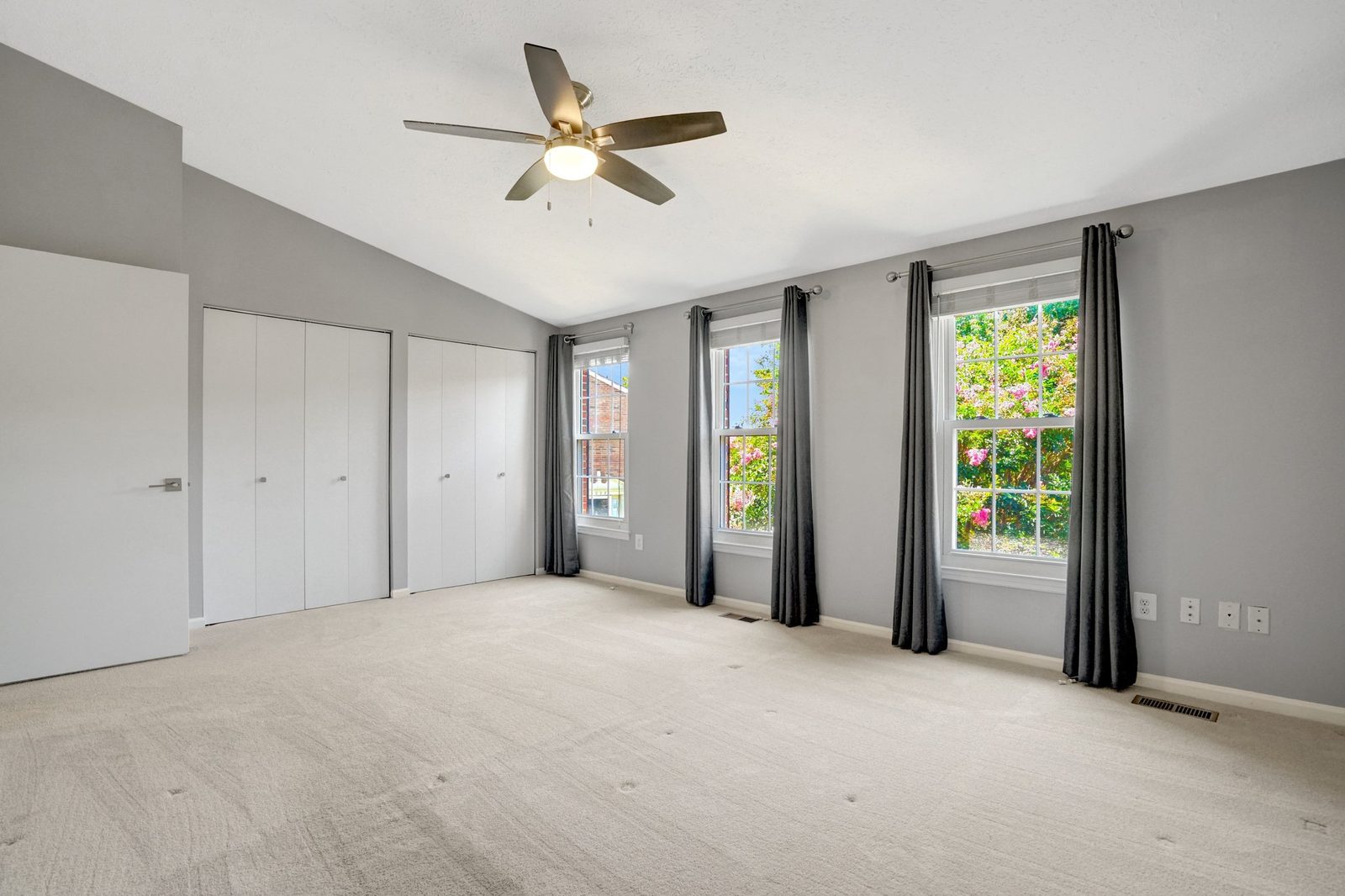Bright carpeted room with two closets and three curtained windows