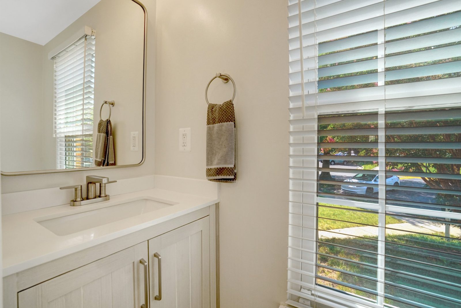 White vanity with mirror, towel ring and blinded window