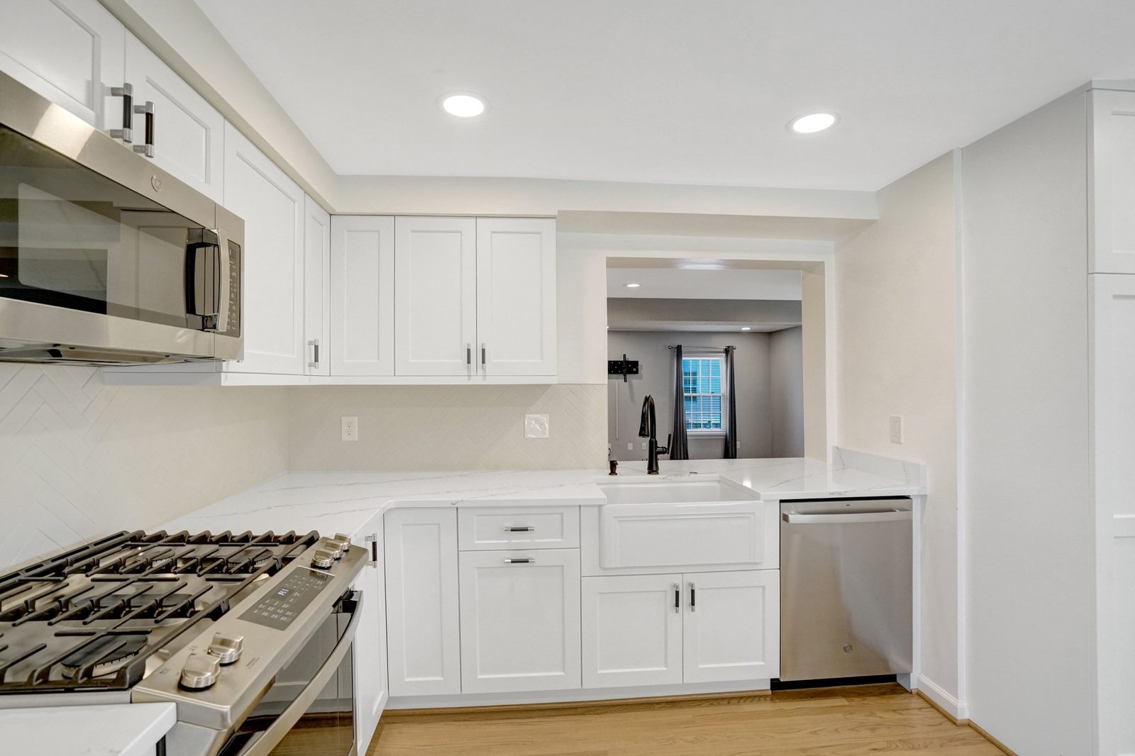 White shaker kitchen with gas range, apron-front sink and stone-look counters