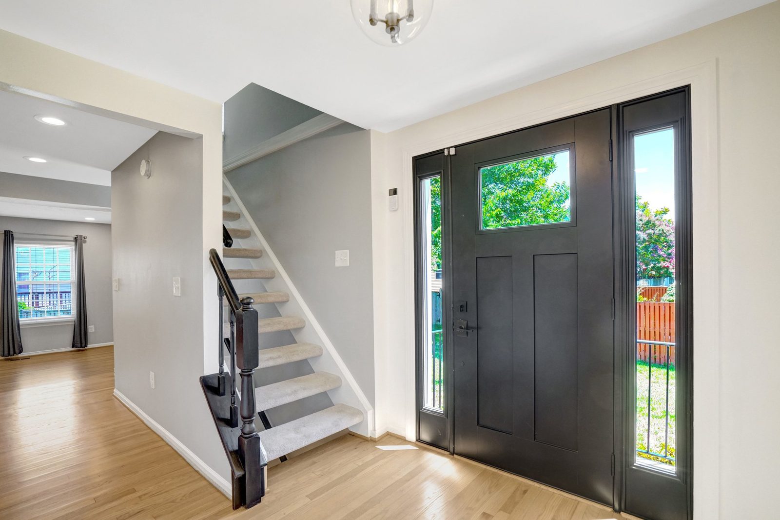 Foyer with hardwood floors, black front door and carpeted staircase
