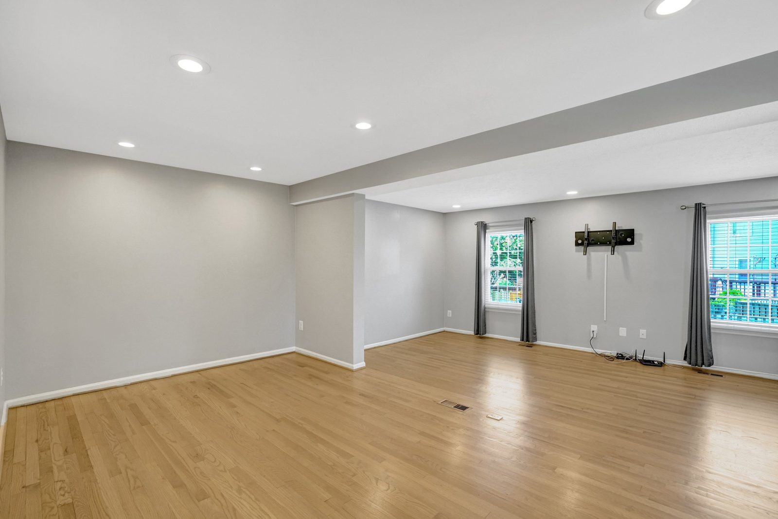 Open living room with hardwood floors, gray walls and two curtained windows