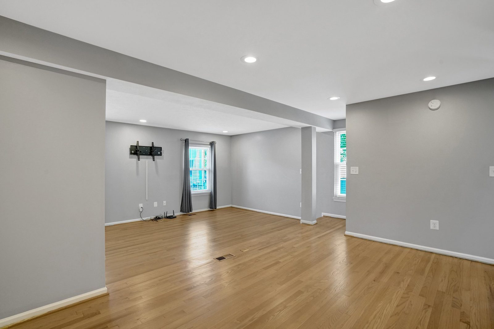 Open room with hardwood floors, curtained window and wall-mounted TV bracket