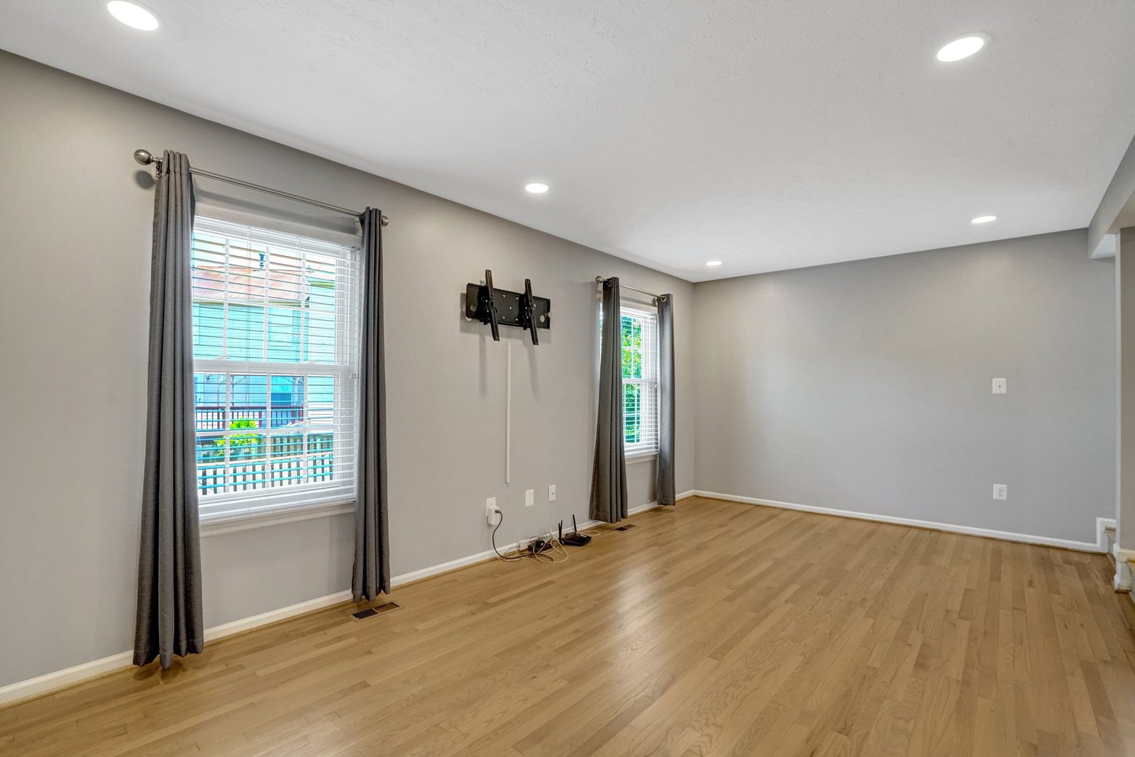 Gray room with hardwood floors, two curtained windows and TV bracket