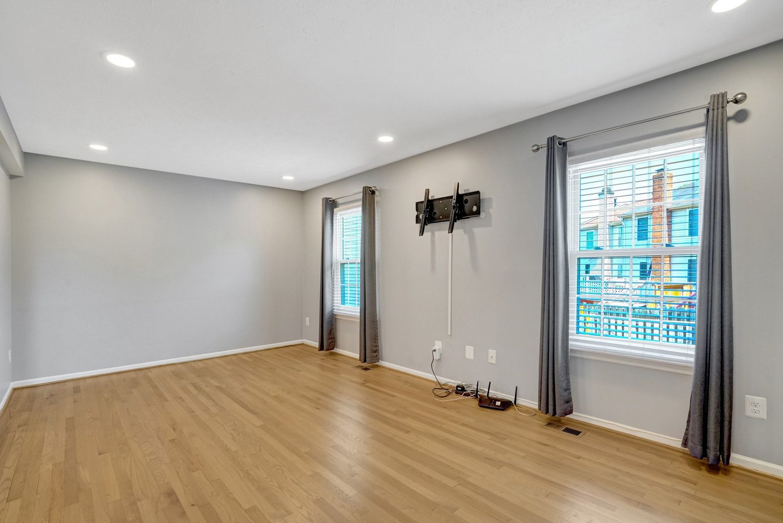 Hardwood room with two curtained windows and wall-mounted TV bracket