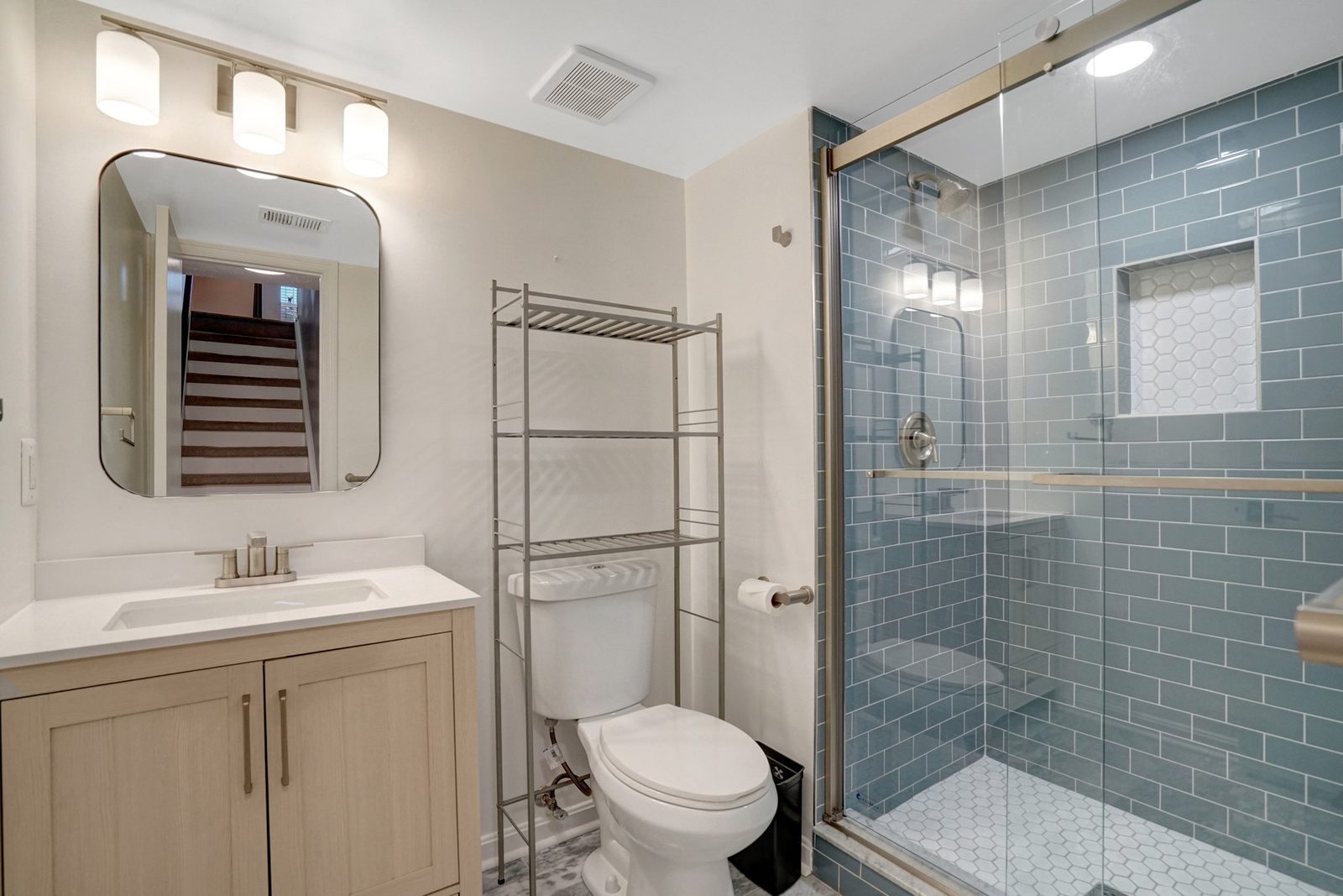 Bathroom with light wood vanity, glass shower and blue subway tile