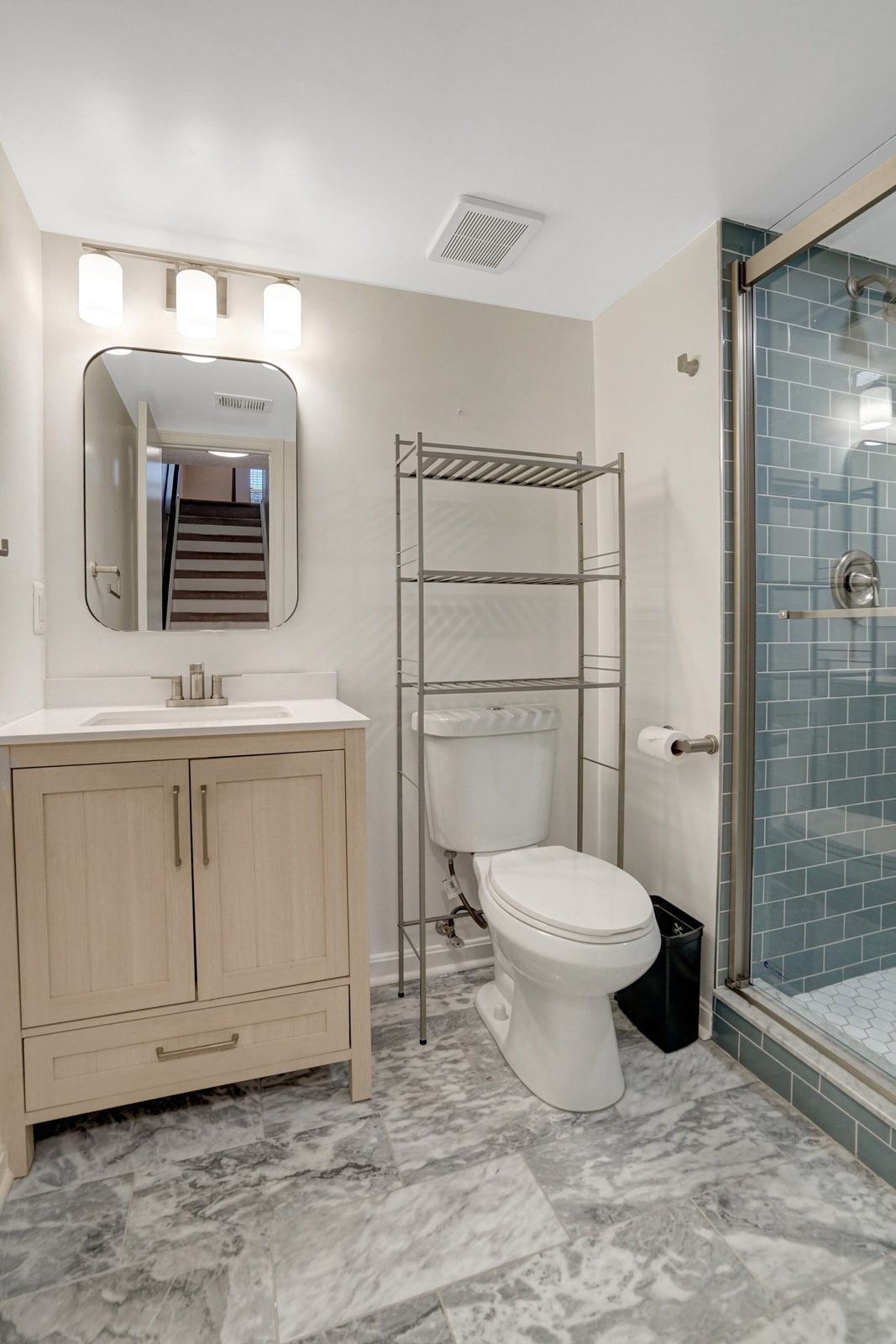 Bathroom with wood vanity, marble-look tile floor and glass shower