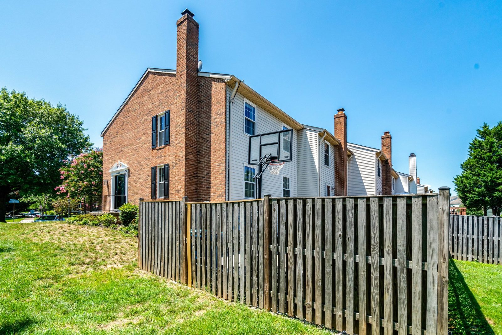 Fenced side yard beside brick and vinyl townhouse row with lawn