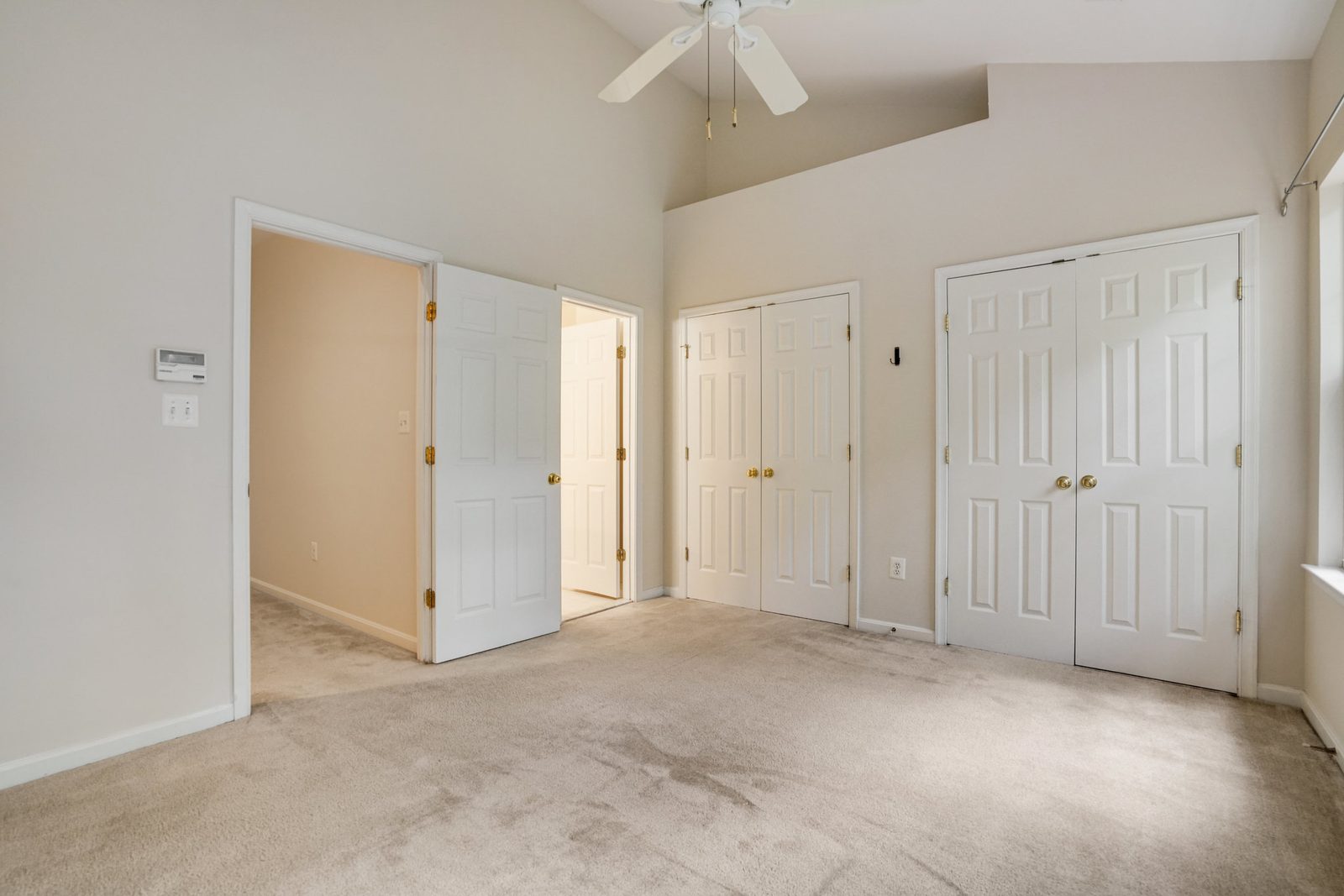 Carpeted room with vaulted ceiling, ceiling fan and double closet doors