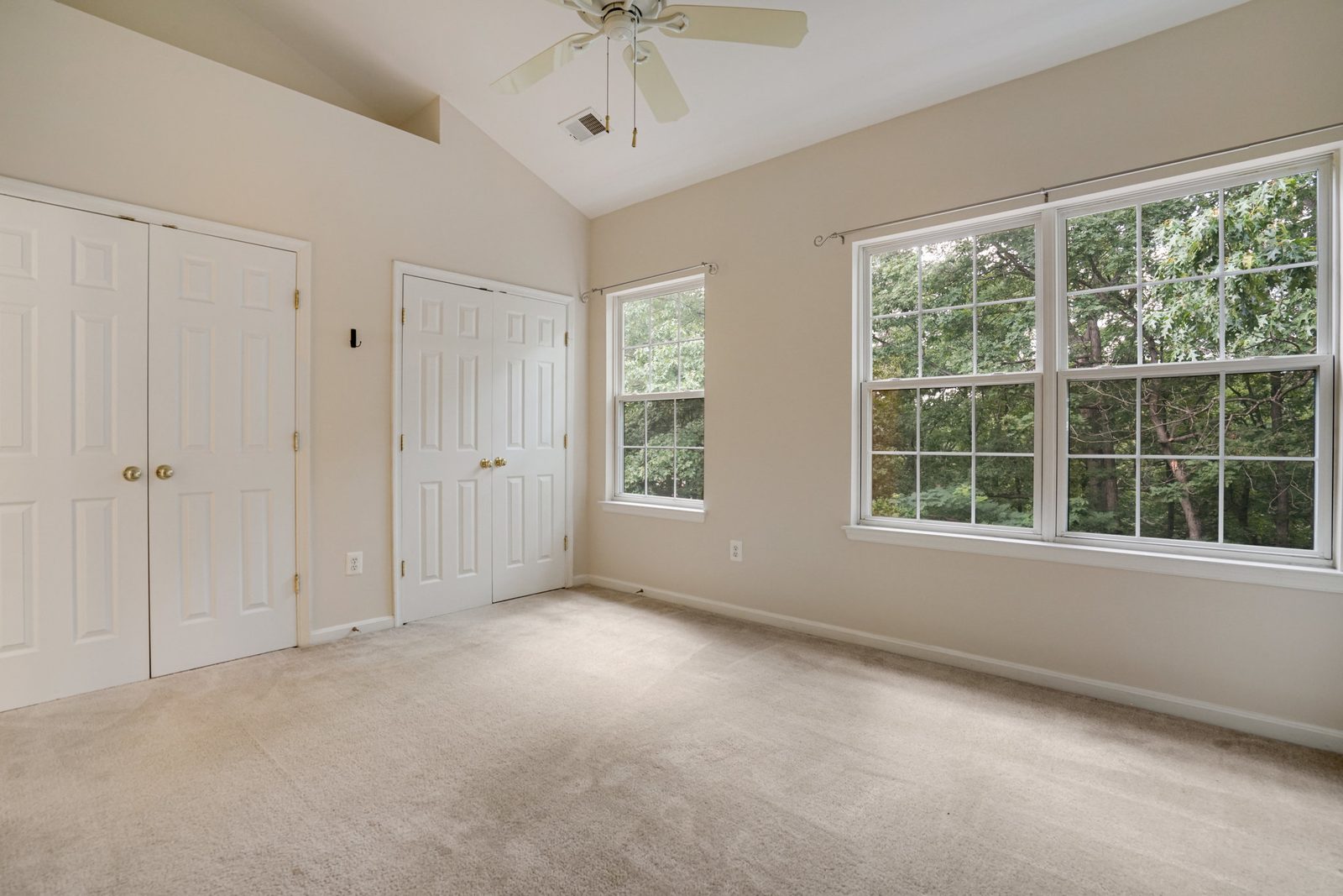 Carpeted room with vaulted ceiling, two closets and windows overlooking trees