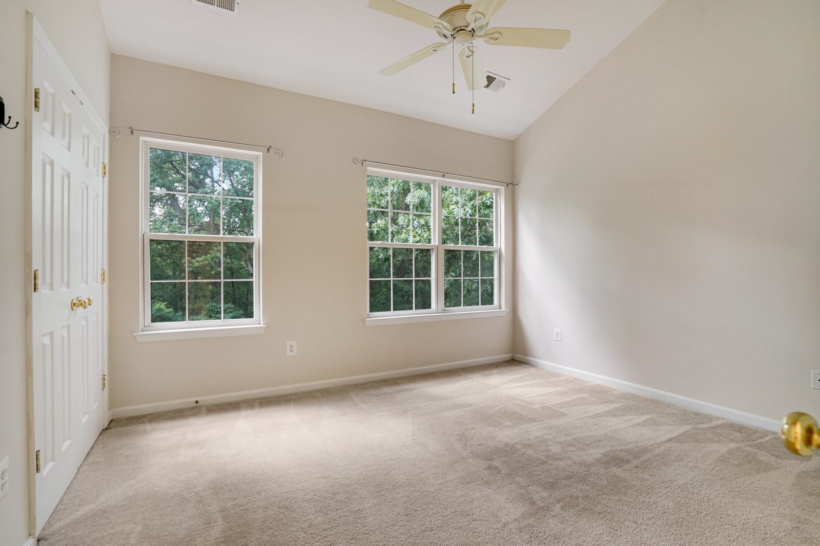 Carpeted room with vaulted ceiling and windows framing green treetops