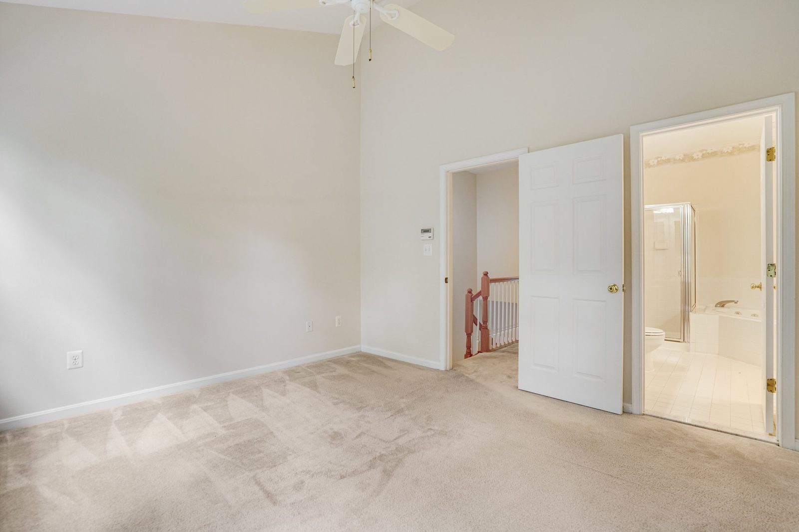 Carpeted room with vaulted ceiling opening to tiled bathroom and stair landing