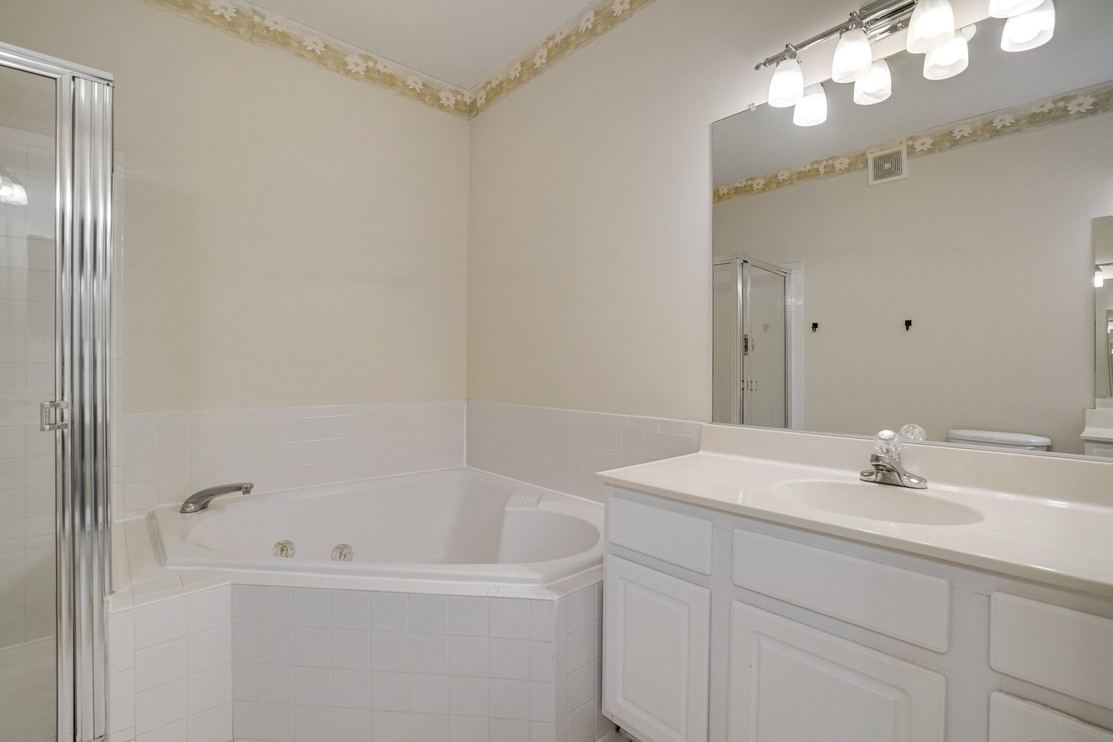 Corner jetted tub, tiled surround and single vanity with wide mirror