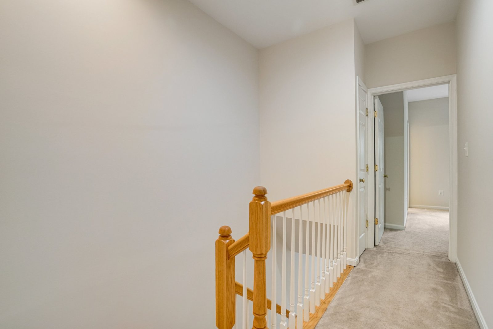 Upstairs landing with oak handrail, white balusters and carpeted floor