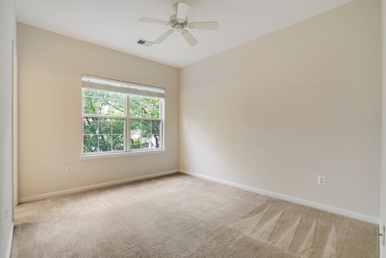 Carpeted room with ceiling fan and single window with blinds