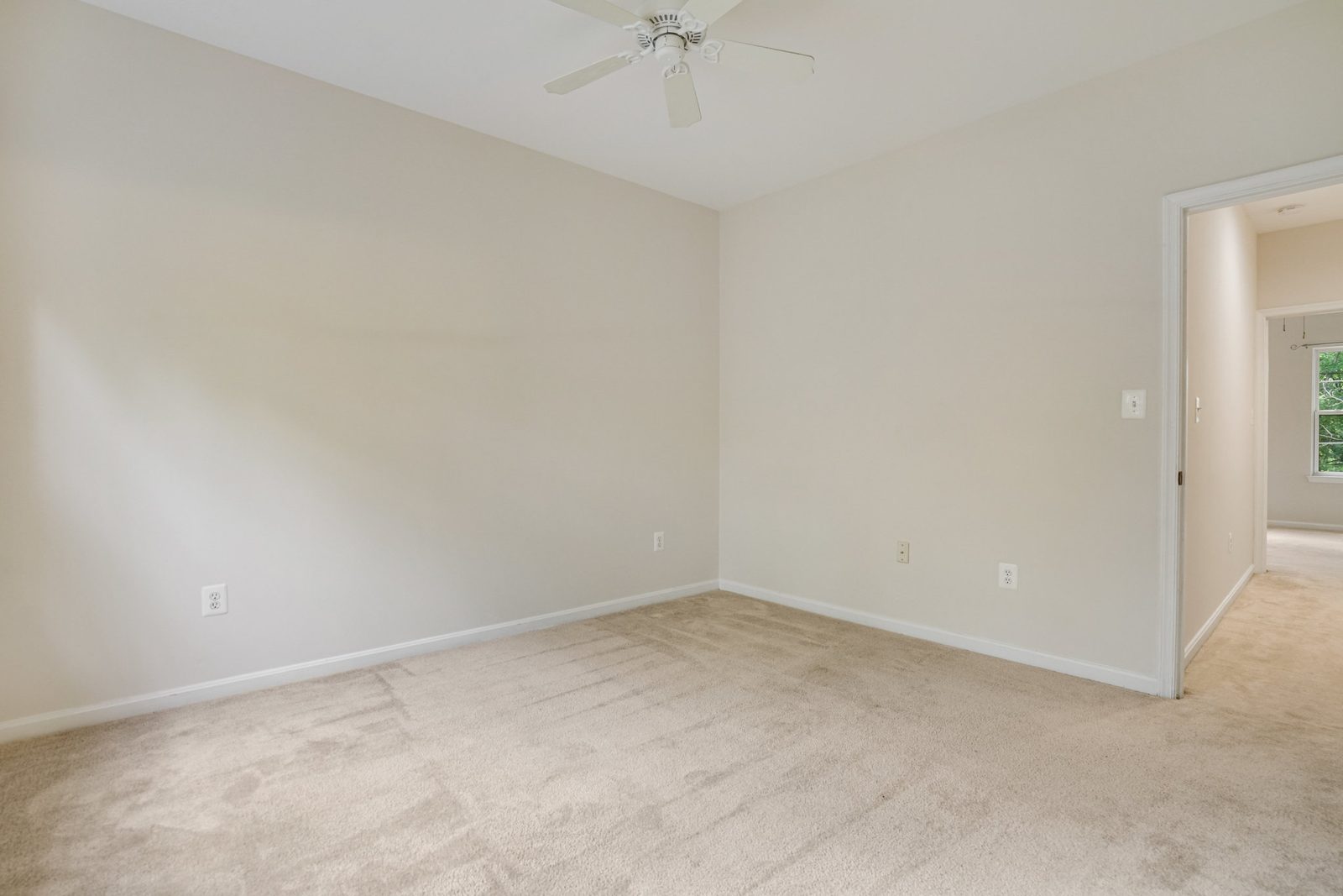 Carpeted room with ceiling fan and doorway to lit hallway