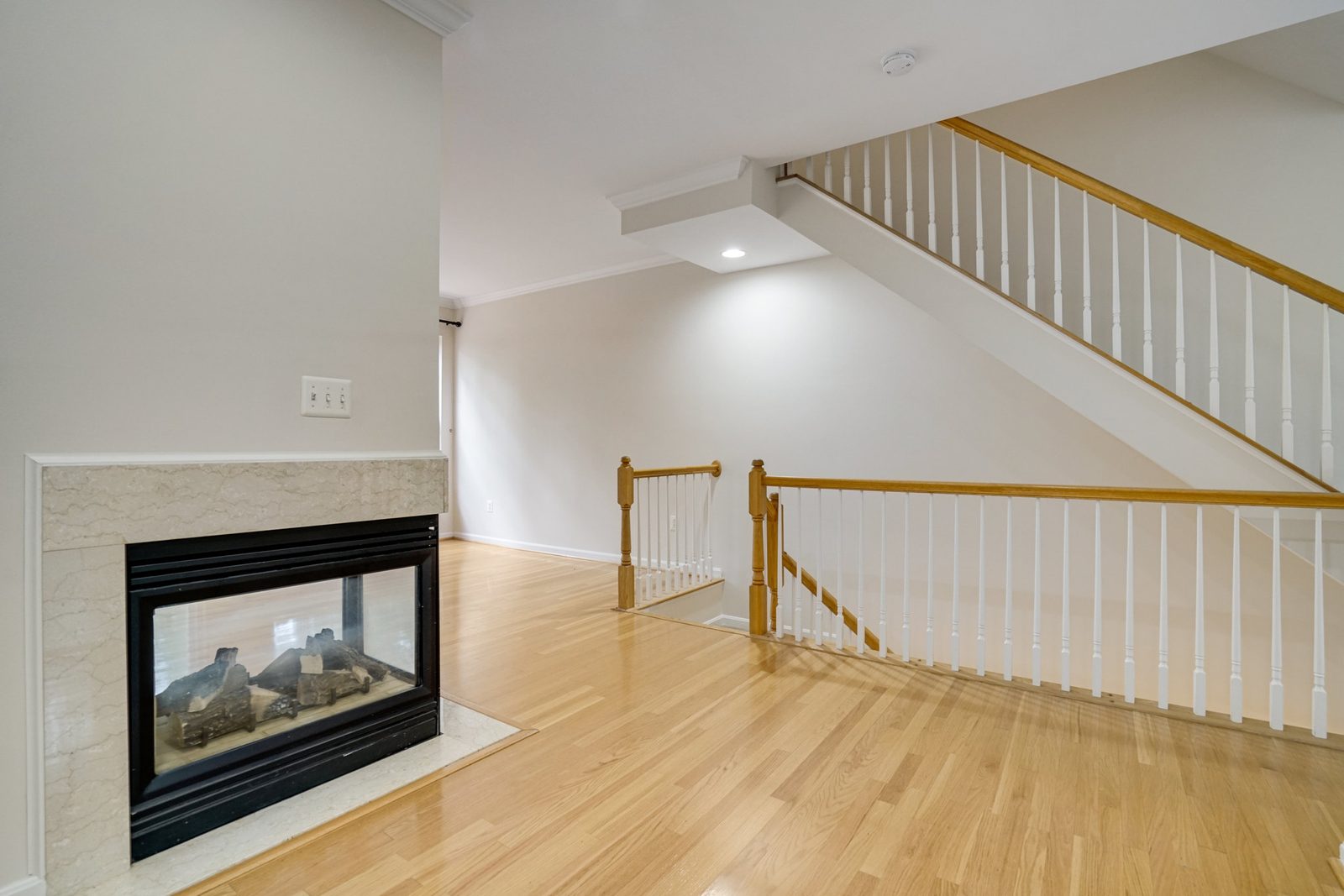 Hardwood living area with three-sided fireplace and oak stair railing