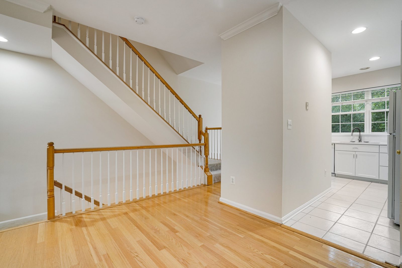 Hardwood floors and oak staircase beside tiled kitchen with white cabinets