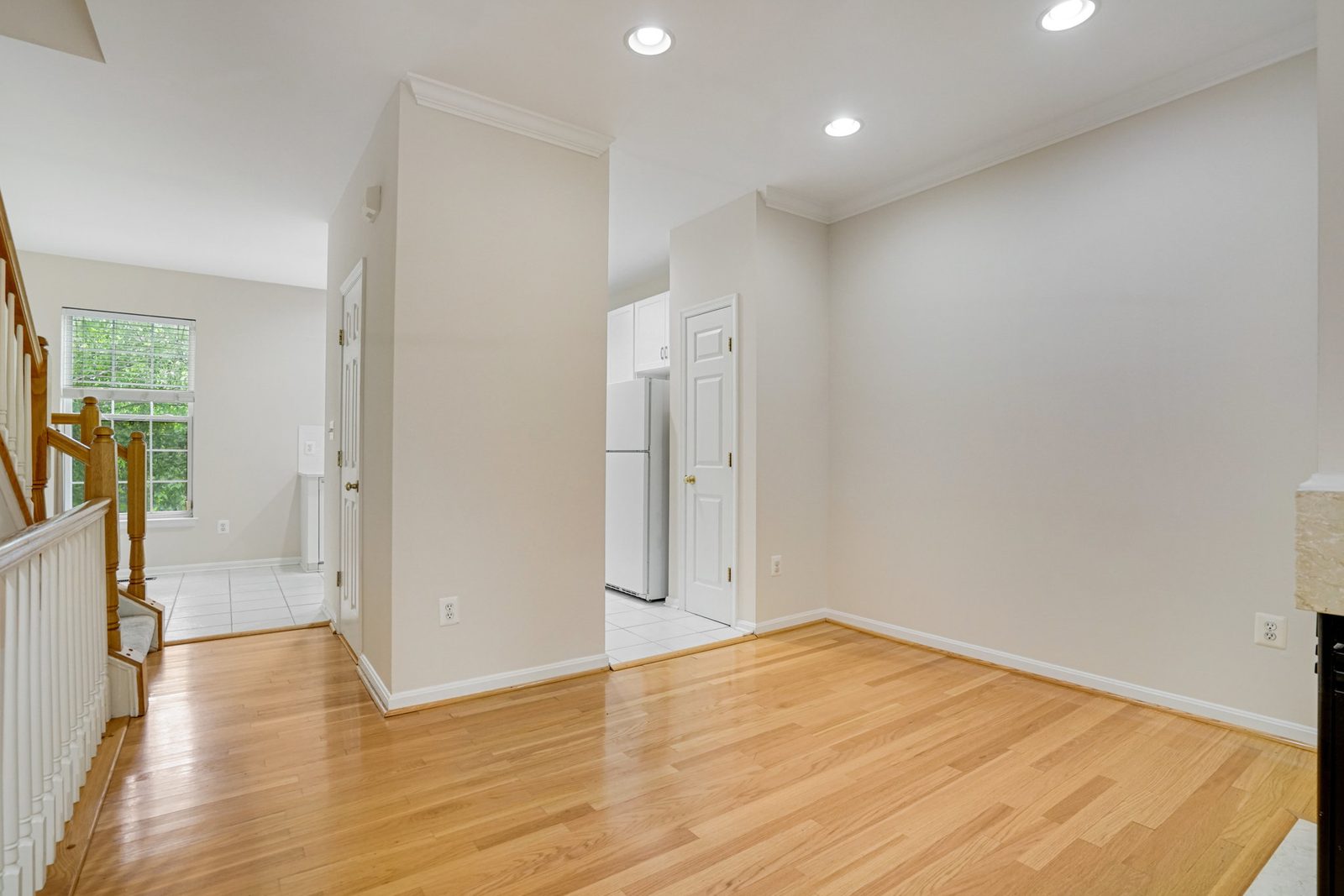 Hardwood room with crown molding beside tiled kitchen and staircase