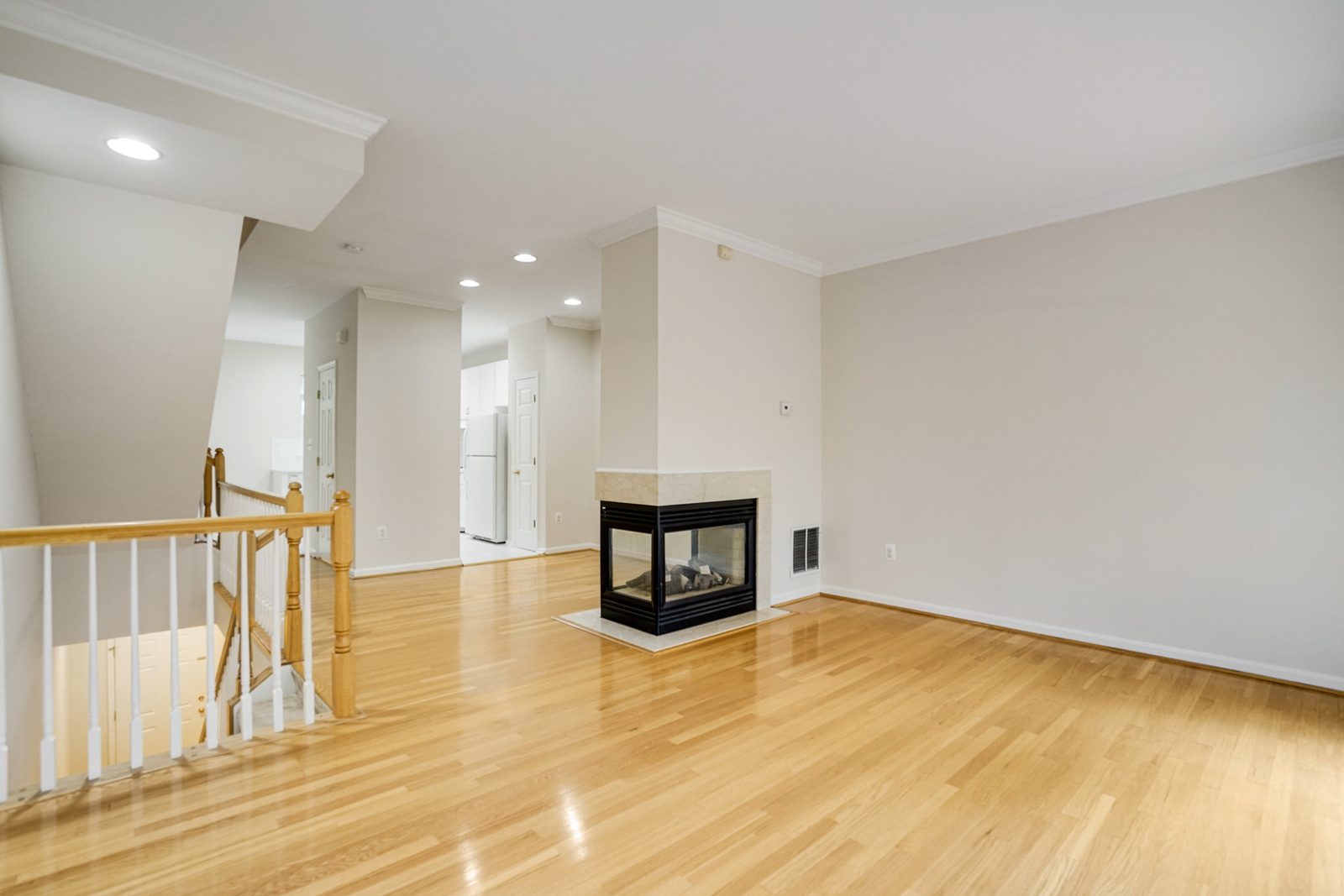 Open hardwood living area with corner three-sided fireplace