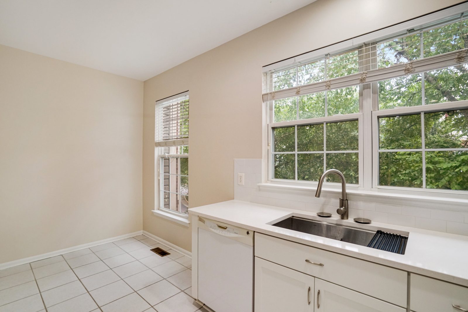 Kitchen sink under twin windows with dishwasher and tile floor