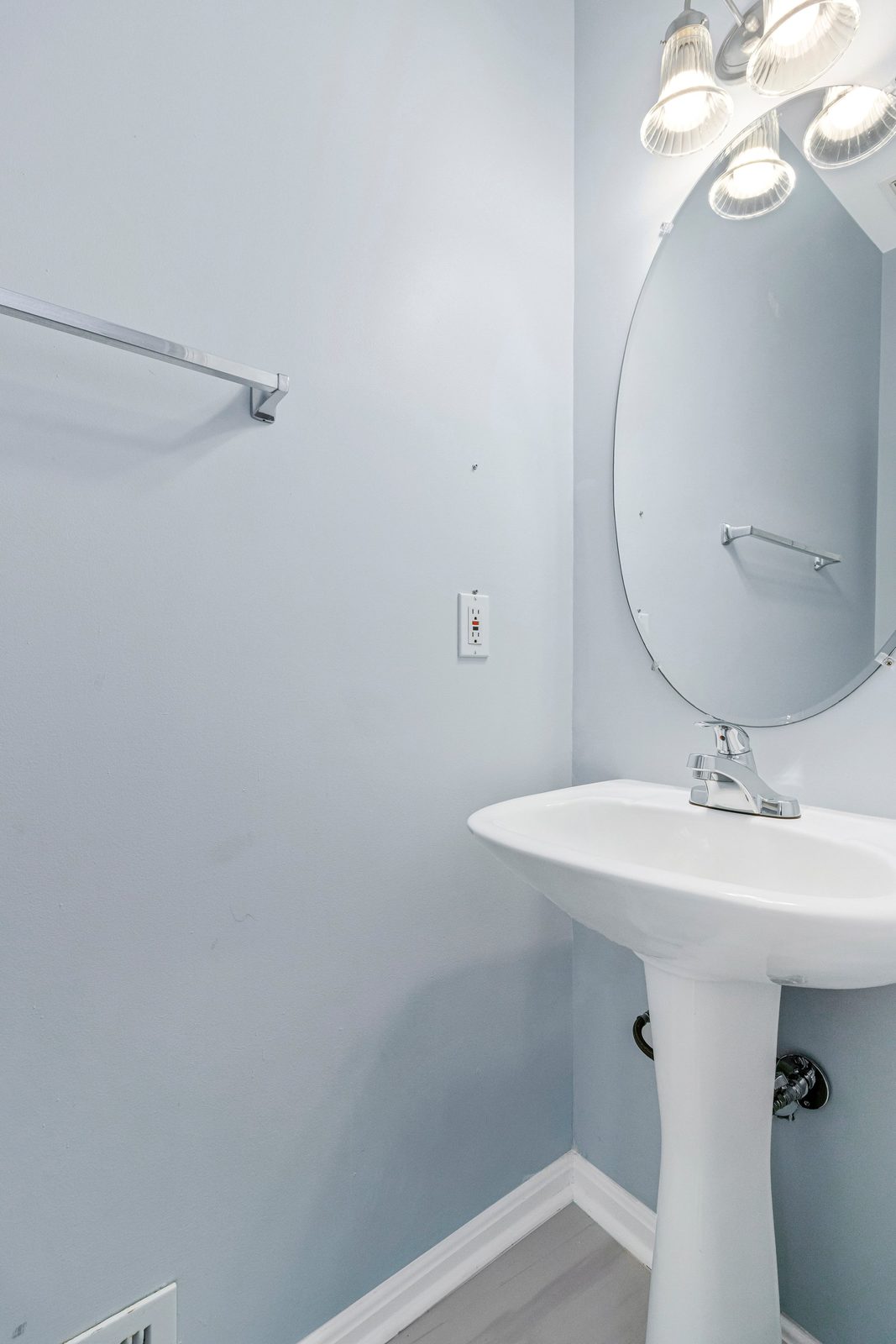 Pedestal sink and oval mirror in pale blue powder room