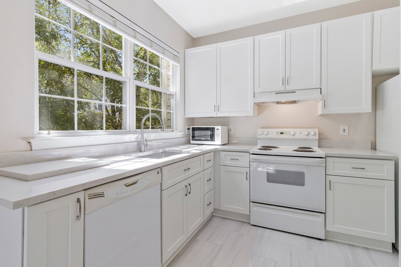 Kitchen with white dishwasher, sink under window and tile floor