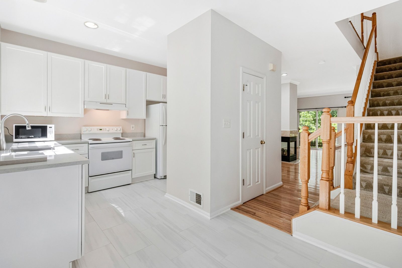 White kitchen with electric range opening to hardwood hall and staircase