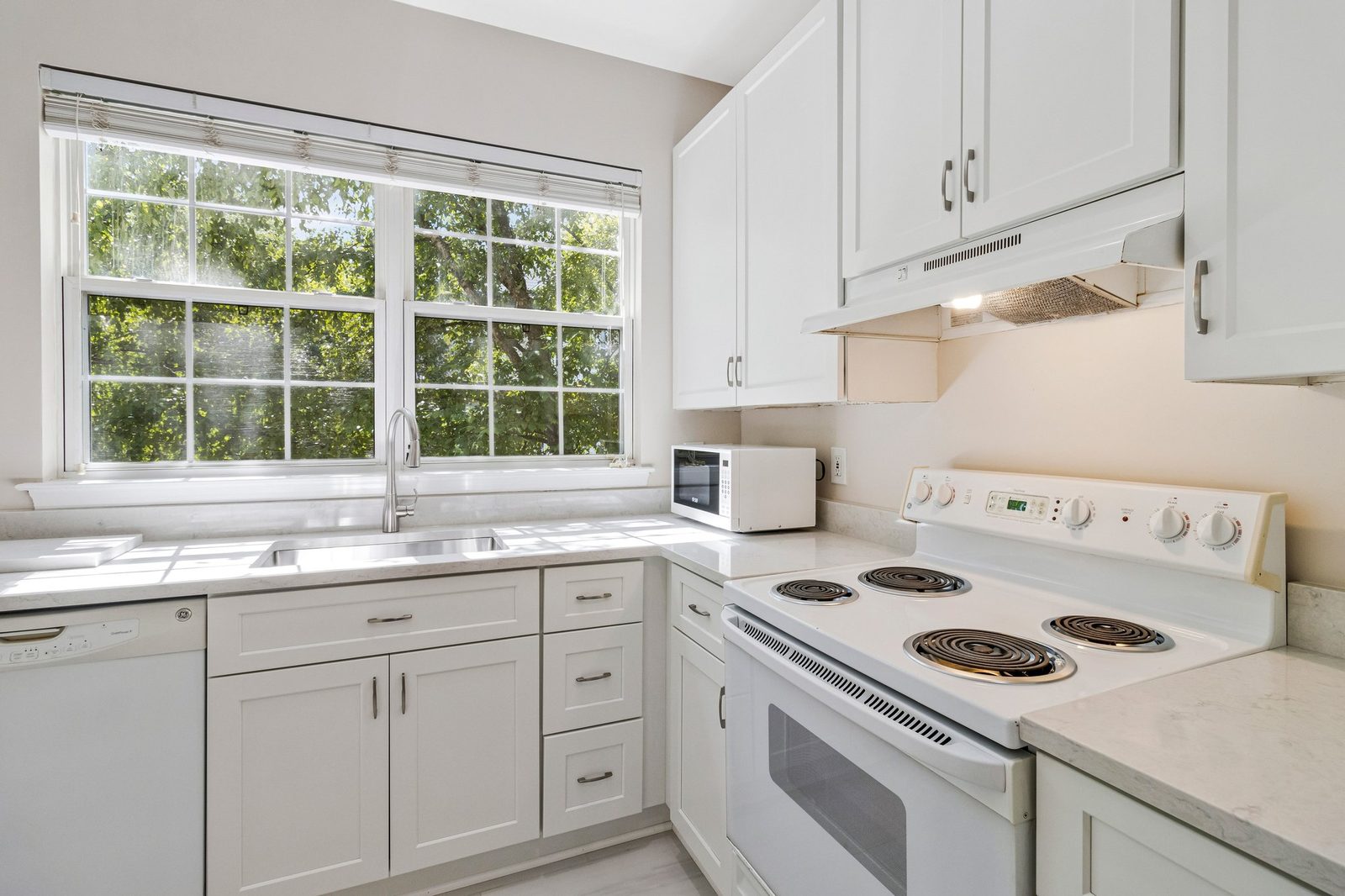 Kitchen with stainless sink under window, white cabinets and electric range