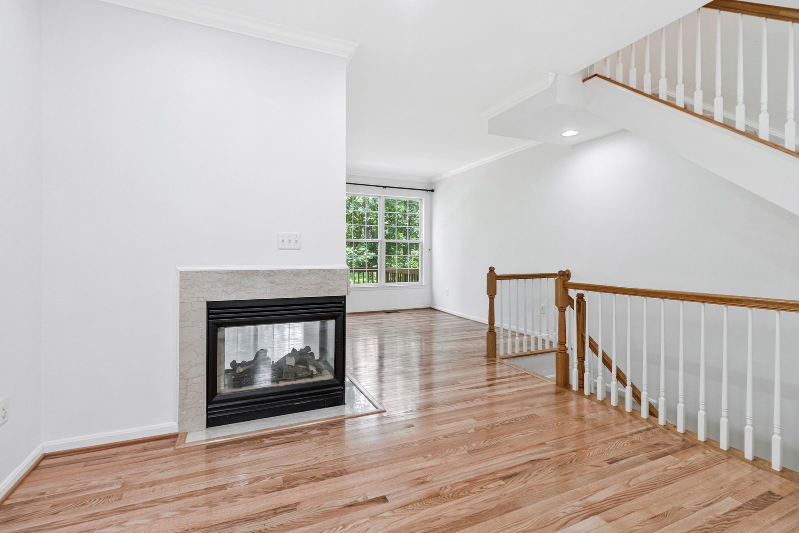 Empty room with three-sided gas fireplace and hardwood floors