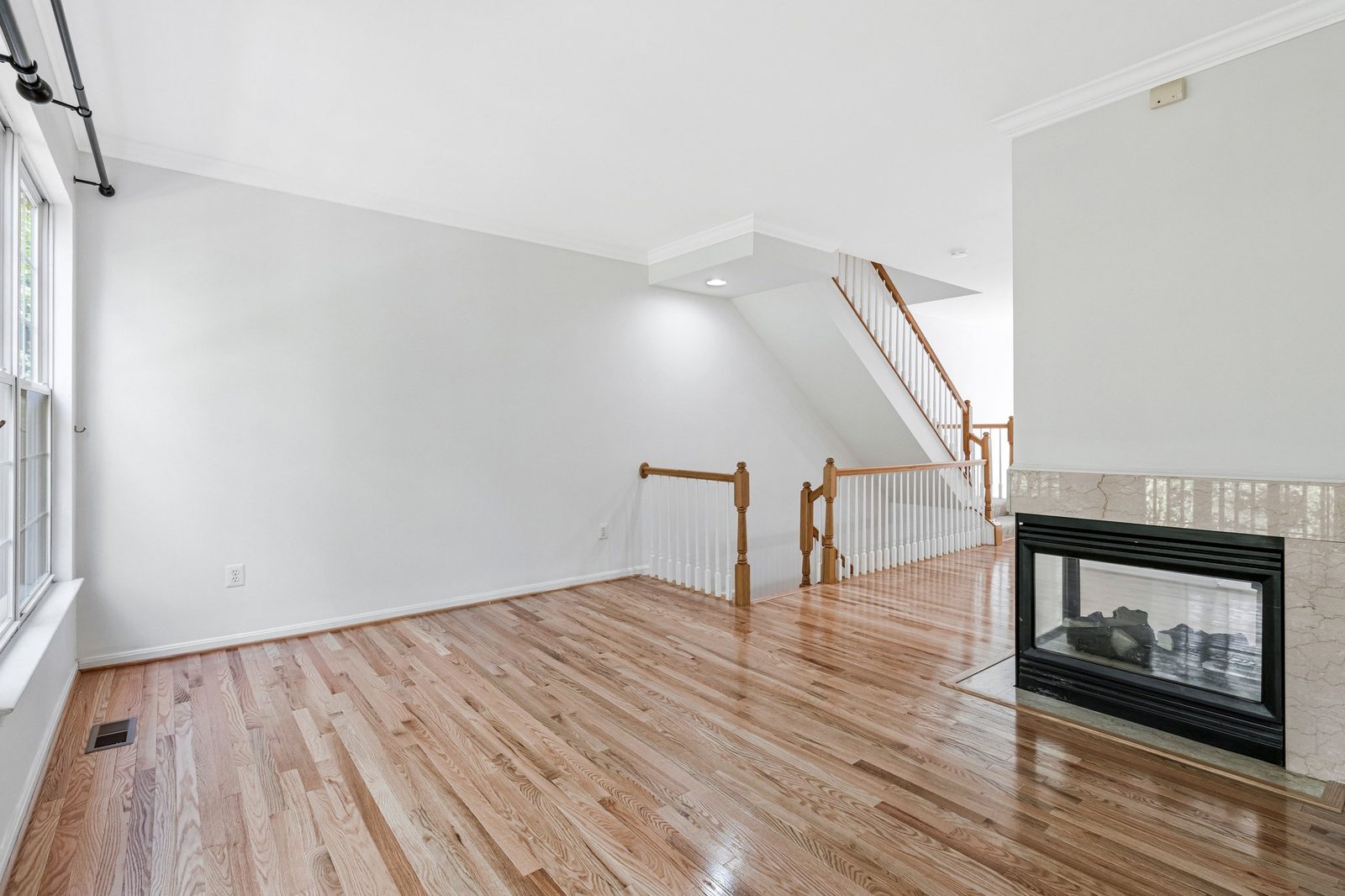 Hardwood room with stair railing and stone-surround gas fireplace
