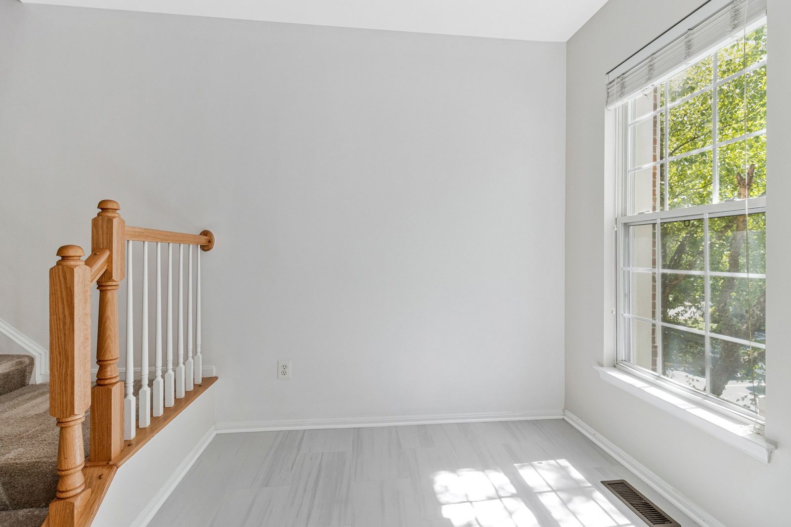 Tiled area beside stair railing with tall window and blinds